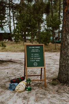 a sign sitting in the sand next to a tree and some camping gear on it