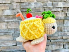 a hand holding a small crocheted cupcake with fruit on top and candy in the middle