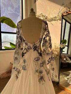 a white dress with blue flowers is on display in front of a mirror and some plants