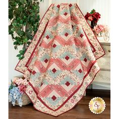 a pink and blue quilt sitting on top of a wooden floor next to a potted plant