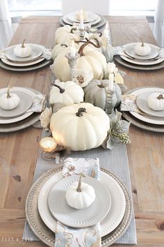 the table is set with white pumpkins and silver plates, candlesticks and napkins