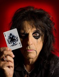 a man with black makeup holding up a playing card