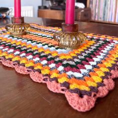 a crocheted placemat with two candles on it and a pink candle in the middle