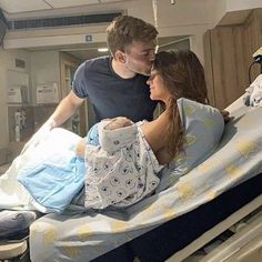 a man standing next to a woman in a hospital bed while she is holding the baby