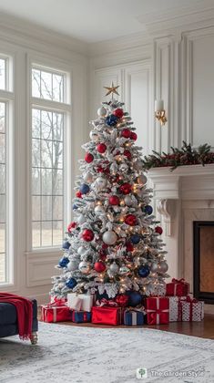 a white christmas tree with red, blue and silver ornaments in front of a fireplace