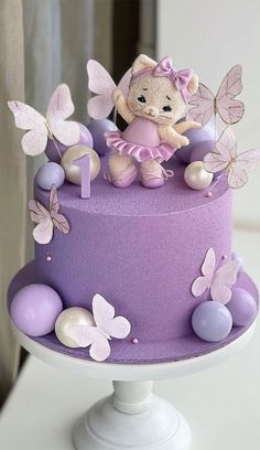 there is a cake decorated with purple and white butterflies on the top, and a teddy bear figurine in the middle