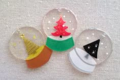 three snow globes with christmas trees and hats in them on a white tablecloth