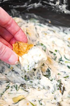 a hand holding a cracker over a bowl of dip with spinach and cheese