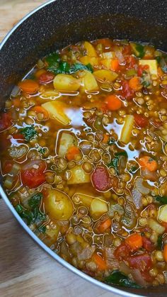 a pot filled with soup and vegetables on top of a wooden table next to a spoon