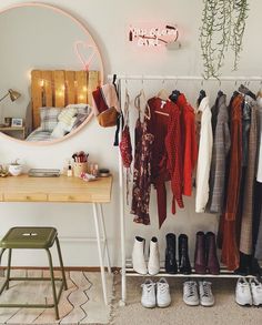 a room with clothes and shoes hanging on the wall, next to a mirror that has lights above it