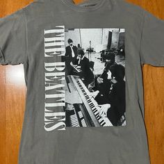 an old t - shirt with the beatles on it sitting on a wooden floor next to a keyboard