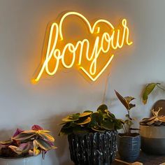 a neon sign that says bonjou on the side of a wall next to potted plants