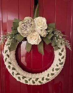 a crocheted wreath with white flowers and greenery hangs on a red door