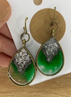 a pair of earrings with green and silver glittered tears hanging from gold - plated hooks