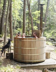 a man and two children in a wooden hot tub with a dog standing next to it