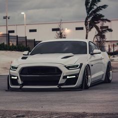 the front end of a white car parked in a parking lot next to a building