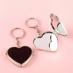 two heart shaped mirrors sitting next to each other on a pink surface, one has a keychain and the other has a mirror