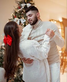 a man and woman standing in front of a christmas tree with a red bow on their head