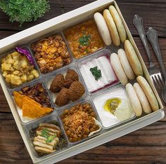 an open lunch box filled with different foods and utensils on top of a wooden table