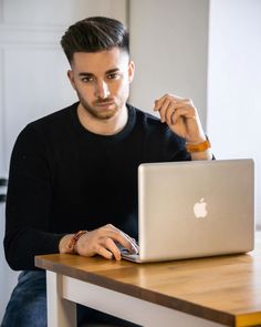 a man sitting at a table working on his apple laptop with the keyboard and mouse in front of him