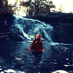 a woman is in the water near a waterfall