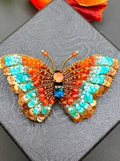 a colorful butterfly brooch sitting on top of a piece of cloth next to an orange flower