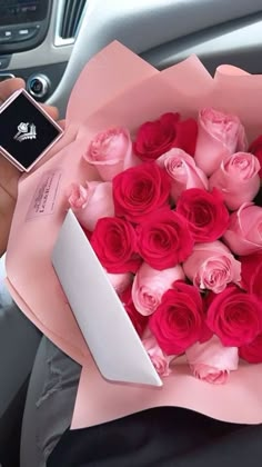 a person holding a bouquet of pink and red roses in their hand with a cell phone