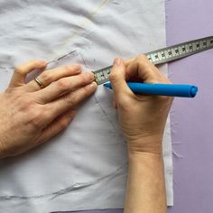 two hands are holding a blue plastic ruler and measuring it with one hand, while the other is on top of a piece of paper