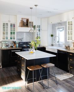 a kitchen with black and white cabinets, an island table and stools in the center