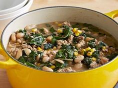 a yellow pot filled with meat and vegetables on top of a wooden table next to a white plate