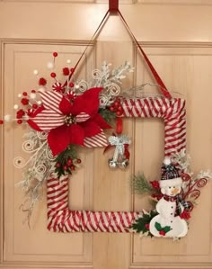 a christmas wreath hanging on the front door with a snowman and candy canes