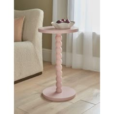 a pink table with a bowl on it in front of a chair and window sill