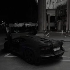 a black sports car parked in the middle of a parking lot at night with its doors open