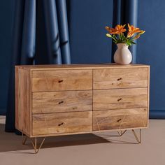 a vase with flowers sitting on top of a wooden dresser