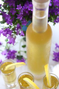 two glasses filled with lemonade next to a bottle and purple flowers in the background