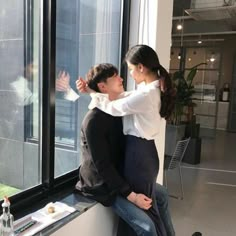 a man and woman sitting on a window sill looking out at the city outside