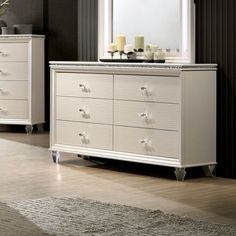 a white dresser sitting next to a mirror on top of a wooden floor