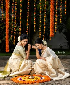 two women sitting next to each other in front of an orange and yellow flower arrangement