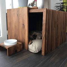 a dog is sleeping in his kennel on the floor next to a bowl and potted plant