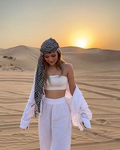 a woman standing on top of a sandy beach next to a sun set in the background