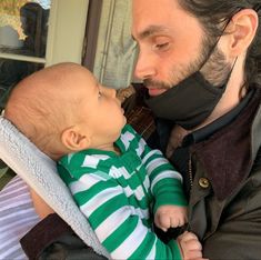 a man holding a baby in his arms and wearing a face mask to protect him from the sun