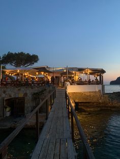 people are sitting at tables on the dock by the water as the sun goes down