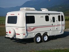 an rv is parked on the side of the road in front of mountains and grass