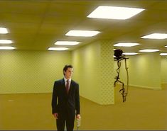 a man in a suit and tie standing in an empty room next to a camera