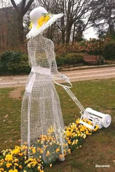 a woman with a lawn mower and flowers in front of her, on the grass