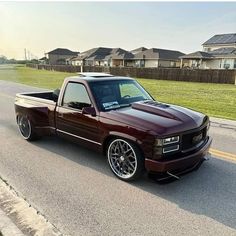 a maroon pick up truck parked on the side of the road in front of some houses