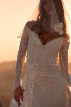 a woman in a wedding dress with a veil over her head and the sun behind her