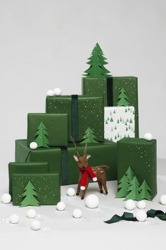 a reindeer is standing in front of green presents with white balls on them and snow around it