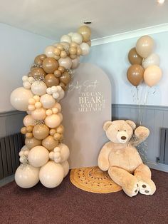 a teddy bear sitting next to a tall balloon arch with balloons on it's sides