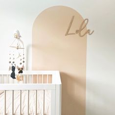 a baby crib in a white room with a wooden name on the wall